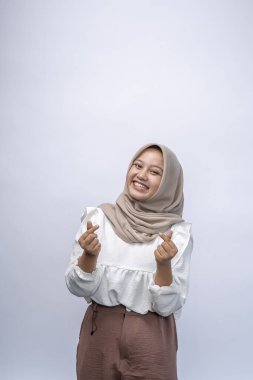 Güzel, güler yüzlü, Endonezyalı, tesettürlü, tesettürlü Müslüman kadın beyaz arka planda izole edilmiş Kore aşk işareti gösteriyor. İnsanlar dini yaşam tarzı konsepti