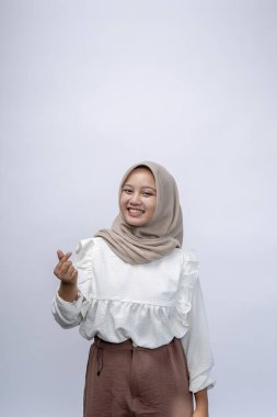 Güzel, güler yüzlü, Endonezyalı, tesettürlü, tesettürlü Müslüman kadın beyaz arka planda izole edilmiş Kore aşk işareti gösteriyor. İnsanlar dini yaşam tarzı konsepti