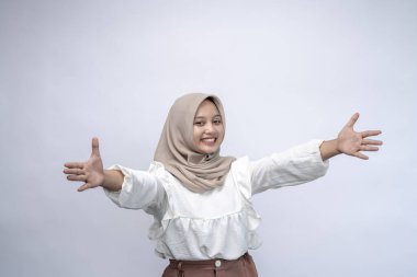 Sarıl bana. Kamera karşısında tesettürlü genç Endonezyalı kadın portresi, Beyaz arka planda soyutlanmış bir şekilde dururken Mutlu Gülümseyen Milenyum Kadın Kolları Kucaklaşmak, Boşluğu Kopyalamak