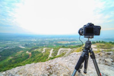 Tripodun üzerinde modern profesyonel kamera, vahşi hayatta açık hava fotoğrafçılığı. Dağların arkaplanı.