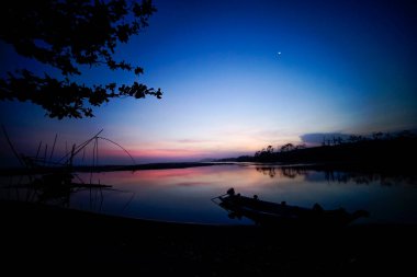 Gölde öğleden sonra atmosferi. Tekne silueti ve manuel balık bulucusuyla.