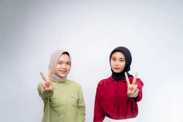 Peace. Portrait of two young asian woman wearing hijab raised two fingers at Copy Space Advertising Your Text, Standing Isolated Over white Studio Background