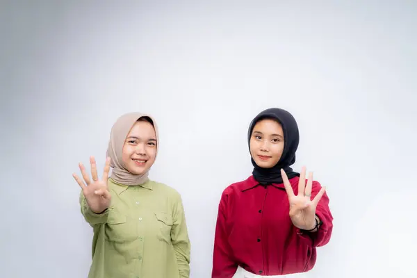 Number four. Portrait of two young asian woman wearing hijab Use your fingers to symbolize the number four at Copy Space Advertising Your Text, Standing Isolated Over white Studio Background