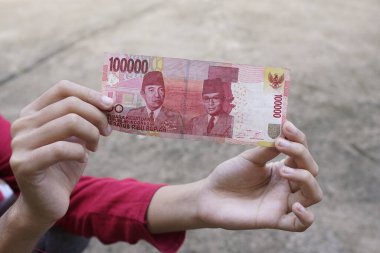 Kadın yüz bin rupiah gösteriyor.