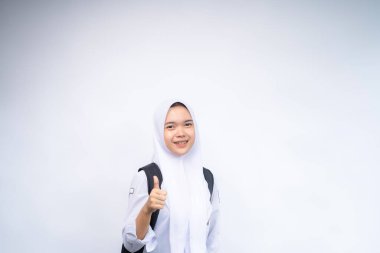 Beyaz ve gri üniformalı Endonezyalı kız lise öğrencisi gülümsüyor ve tamam işareti gösteriyor.