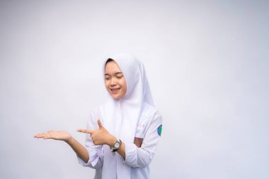 Heyecanlı Endonezyalı beyaz ve gri üniformalı lise öğrencisi, yanındaki fotokopi alanını işaret ediyor, beyaz arka planla izole edilmiş.