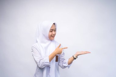 Heyecanlı Endonezyalı beyaz ve gri üniformalı lise öğrencisi, yanındaki fotokopi alanını işaret ediyor, beyaz arka planla izole edilmiş.