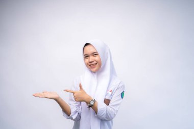 Heyecanlı Endonezyalı beyaz ve gri üniformalı lise öğrencisi, yanındaki fotokopi alanını işaret ediyor, beyaz arka planla izole edilmiş.