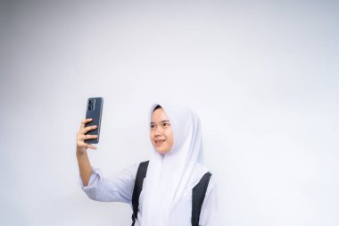 Beyaz ve gri üniformalı genç ve güzel bir bayan cep telefonu kullanarak selfie çekiyor.