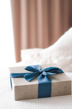 Holiday present and luxury online shopping delivery, wrapped linen gift box with blue ribbon on bed in bedroom, chic countryside style, close-up