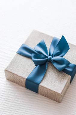 Holiday present and luxury online shopping delivery, wrapped linen gift box with blue ribbon on bed in bedroom, chic countryside style, close-up