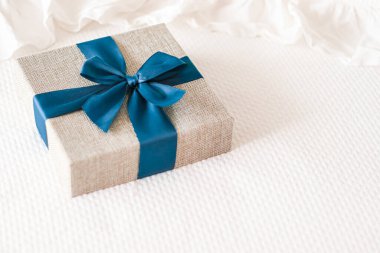 Holiday present and luxury online shopping delivery, wrapped linen gift box with blue ribbon on bed in bedroom, chic countryside style, close-up