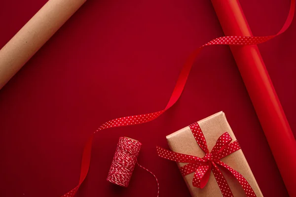 Gifts preparation, birthday and holidays gift giving, craft paper and ribbons for gift boxes on red background as wrapping tools and decorations, diy presents as holiday flat lay design.