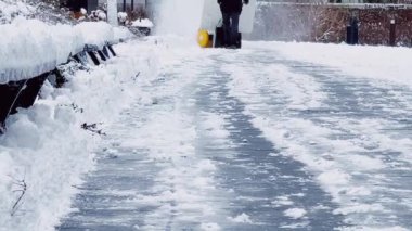 Snowing weather conditions, unrecognisable man using snow removal machine to clean the sidewalk in winter.
