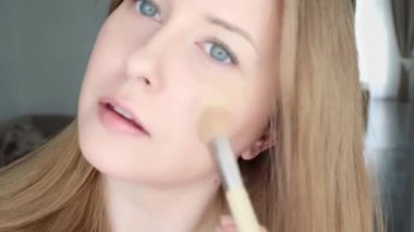 Beautiful blonde woman applying liquid make-up foundation on her skin with makeup brush.