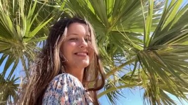 Happy young woman on holidays in summer, smiling girl, palm trees and blue sky.