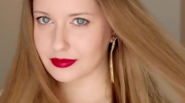 Uzun altın küpeler takan, gülümseyen, kırmızı ruj süren zarif bir kadın.