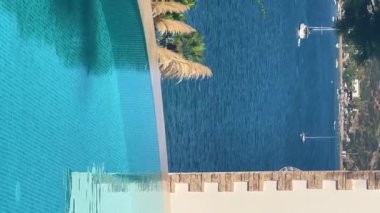 Lüks villa deniz tatil köyünde sonsuz yüzme havuzu manzarası, durgun kristal mavi su ve yaz rahatlaması, yavaş çekim video