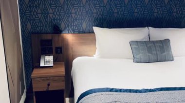 Modern otel odası, modern sanat deco tasarımı, geometrik desenli duvar kağıdı ve dekoratif yastıklı yatak, yavaş çekim video