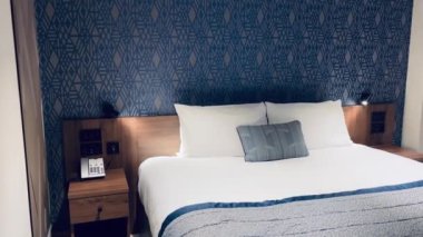 Modern otel odası, modern sanat deco tasarımı, geometrik desenli duvar kağıdı ve dekoratif yastıklı yatak, yavaş çekim video
