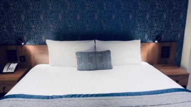 Modern otel odası, modern sanat deco tasarımı, geometrik desenli duvar kağıdı ve dekoratif yastıklı yatak, yavaş çekim video