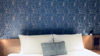Modern otel odası, modern sanat deco tasarımı, geometrik desenli duvar kağıdı ve dekoratif yastıklı yatak, yavaş çekim video