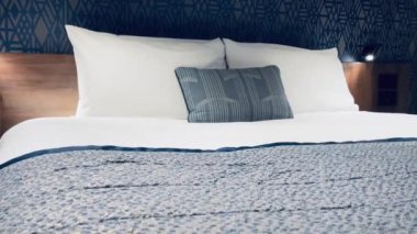 Modern otel odası, modern sanat deco tasarımı, geometrik desenli duvar kağıdı ve dekoratif yastıklı yatak, yavaş çekim video