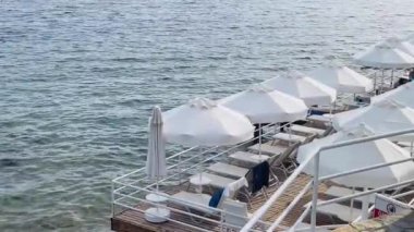 Beyaz plaj şemsiyeleri ve güneşlenme yerleri berrak deniz sularının üzerindeki ahşap iskelede, yaz tatili