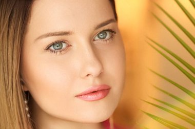 Yaz güzelliği, makyaj ve cilt bakımı, tropik palmiye yaprağı olan güzel bir kadının yüz portresi, kozmetik ve moda için doğal makyaj fikri.