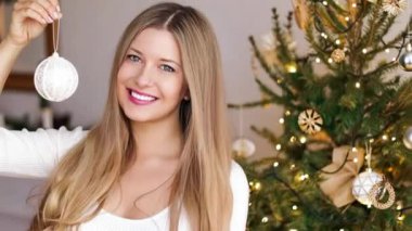 Noel dekorasyonu ve tatil ruh hali konsepti. Mutlu gülümseyen kadın Noel ağacını evde oyuncak ve süslemelerle süslüyor.