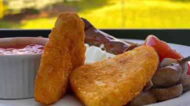 Patates kızartması, mantar, domates, sosis ve fırında fasulye içeren İngiliz kahvaltı tarifi, arka planda manzaralı kırsal bir manzara ile beyaz bir tabakta servis ediliyor. Yüksek kalite 4k görüntü