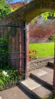 Renkli çiçek yatakları ve budanmış çimen yolları olan güzel manikürlü bir bahçe. Geleneksel İngiliz evleri arka planda, barışçıl ortamı geliştirerek görülebilir. Yüksek kalite 4k görüntü