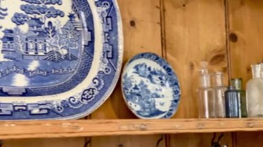 Geleneksel ahşap mutfak şifoniyeri mavi ve beyaz porselen tabaklar ve çay fincanları ile süslenmiş, mükemmel bir İngiliz evinde ılık ve kırsal bir cazibe yaratıyor. Yüksek kalite 4k görüntü