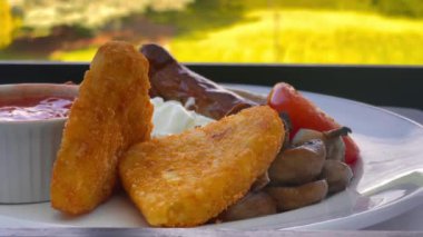 Patates kızartması, mantar, domates, sosis ve fırında fasulye içeren İngiliz kahvaltı tarifi, arka planda manzaralı kırsal bir manzara ile beyaz bir tabakta servis ediliyor. Yüksek kalite 4k görüntü