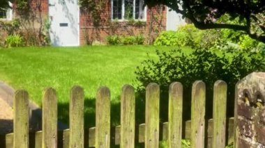 Düzgün bakımlı bir çimen, tuğla dış ve yapraklı ağaçlar çerçeveli beyaz bir kapı ve tuhaf bir İngiliz köyünde tırmanan sarmaşıklar. Yüksek kalite 4k görüntü