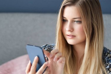 Uzun sarı saçlı ve mavi gözlü bir kadın akıllı telefonuna bakıyor, online alışveriş yapıyor, ev hayatı fikrinden çalışıyor.