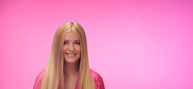 Kadın, pembe arka plan, cazibe ve tarz. Sarışın, güzel bir kadın, uzun saçlı, parlak tenli, moda ve kendine güvenen biri.