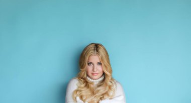 Mavi arka planda kış portresi, sıcak eldivenler giyen mutlu sarışın kadın ve örgü ören, moda ve yaşam tarzı fikri