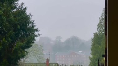 Kırsal İngiltere 'nin barışçıl ve atmosferik cazibesini çağrıştıran, yemyeşil ağaçlar ve çitlerle çerçevelenmiş, kısmen sisli, kırmızı tuğlalı bir binanın bulunduğu puslu kırsal bölge manzarası