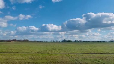 Pofuduk beyaz bulutlarla kaplı parlak mavi gökyüzünün altında geniş bir kırsal alan, doğa yürüyüşleri ve huzur dolu geri çekilmeler için mükemmel barışçıl ve manzaralı bir kırsal alan sunuyor.