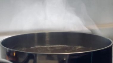 Pürüzsüz bir sobanın üstünde kaynayan bir su tenceresinden çıkan buhar sıcaklığı, sadeliği ve ev yemeği sanatını çağrıştırıyor.