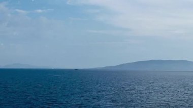 Türkiye 'nin Bodrum kentindeki deniz manzarasında ufka doğru uzanan sakin mavi sular, uzak adalar ve açık gökyüzünde yumuşak, ince bulutlar var.