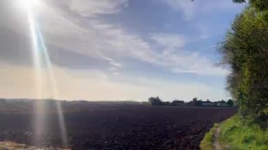 Yumuşak bir ufuk, toprak tonlar ve sessiz bir gökyüzünün altındaki uzak ağaçlar ile engin bir açık alan. Sakin ve kırsal bir çekiciliği çağrıştırıyor.