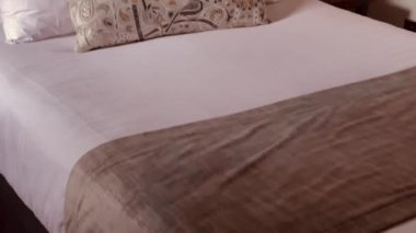 Yumuşak beyaz yastıkları olan rahat bir yatak odası dekoratif bir yastık ve sıcak bir aydınlatma, rahatlatıcı ve davetkar bir atmosfer sunuyor.