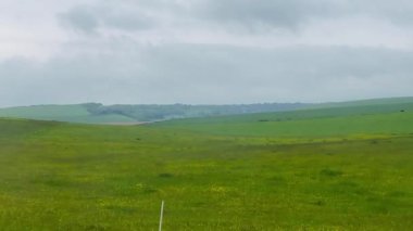 Geniş yeşil alanlar Eastbourne, Doğu Sussex, Birleşik Krallık 'taki kayan tepelere doğru uzanıyor, sakin ve bulutlu bir günde İngiliz kırsalının zamansız cazibesini çağrıştırıyor.