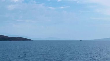 Türkiye 'nin Bodrum kentindeki deniz manzarasında ufka doğru uzanan sakin mavi sular, uzak adalar ve açık gökyüzünde yumuşak, ince bulutlar var.