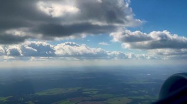 Bir uçak penceresinden hava manzarası engin yeşil alanlar, parlak mavi bir gökyüzü ve dağınık beyaz bulutlar, seyahat ve keşiflerin güzelliğini yakalıyor.