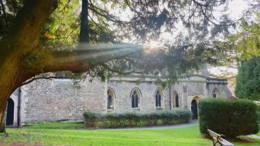 Kemerli pencereleri, taş duvarları ve ağaçlarla çevrili huzurlu bir bahçe yolu dallardan süzülen, dingin ve ebedi bir ortam yaratan İngiliz kırsal kilisesi.
