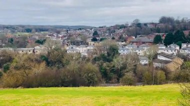 Çevresi yeşilliklerle çevrili beyaz evler ve arka planda yumuşak bulutlu gökyüzü olan huzurlu İngiliz banliyösü manzarası.