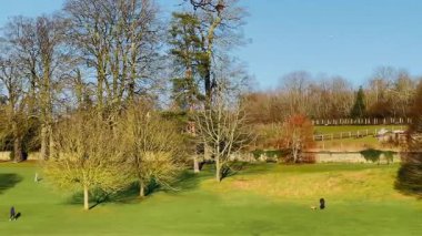 Geniş yeşil çimenler, uzun gölgeler bırakan olgun ağaçlar ve yürümek ve rahatlamak için açık alanlar, İngiliz kırsalının cazibe ve sükunetini somutlaştıran güneş ışığı parkı.